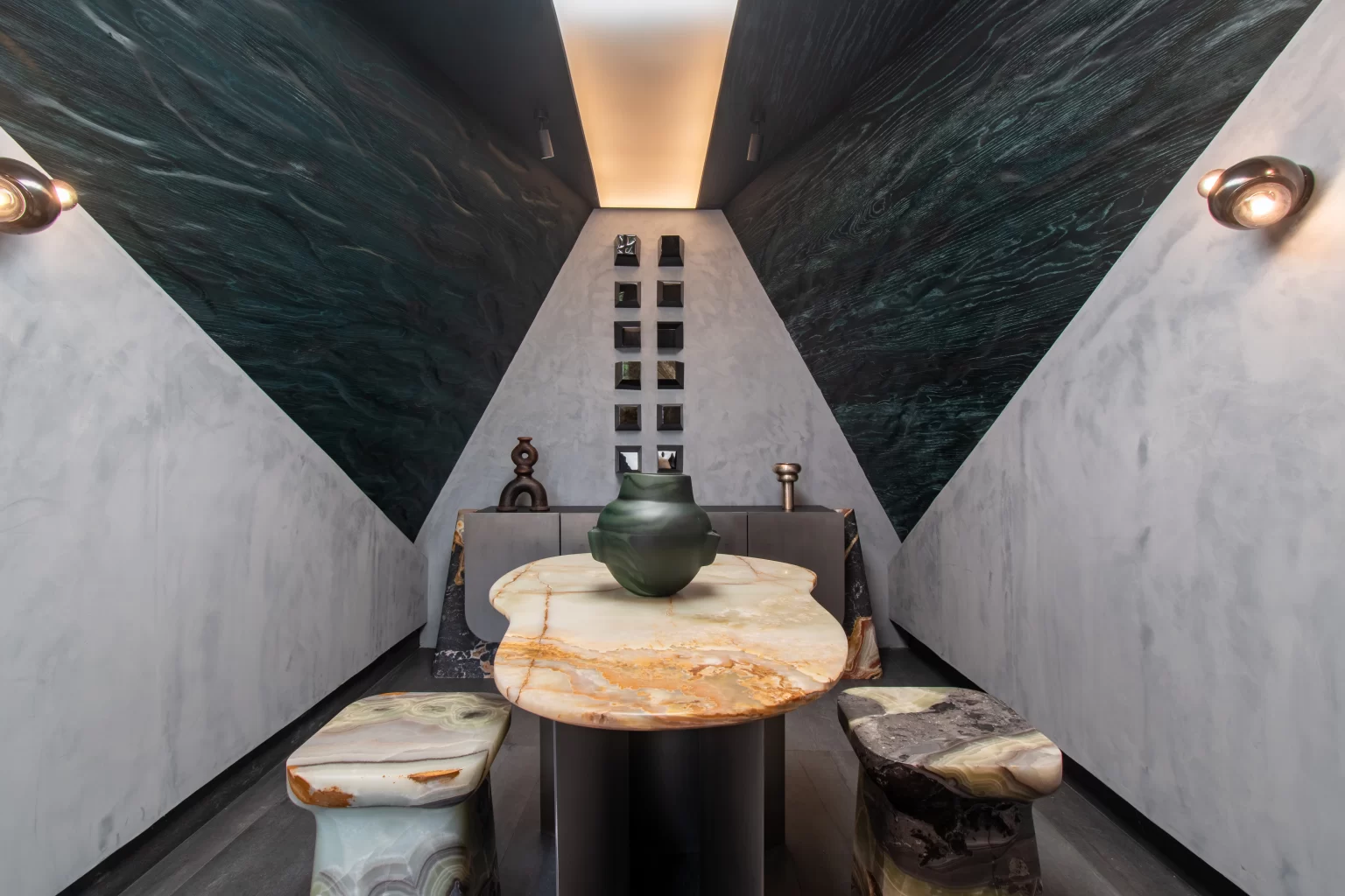 Interior de Santuario Espejo: mesa de ónix iluminada bajo un muro de piedra verde y yeso claro, con piezas de obsidiana empotradas