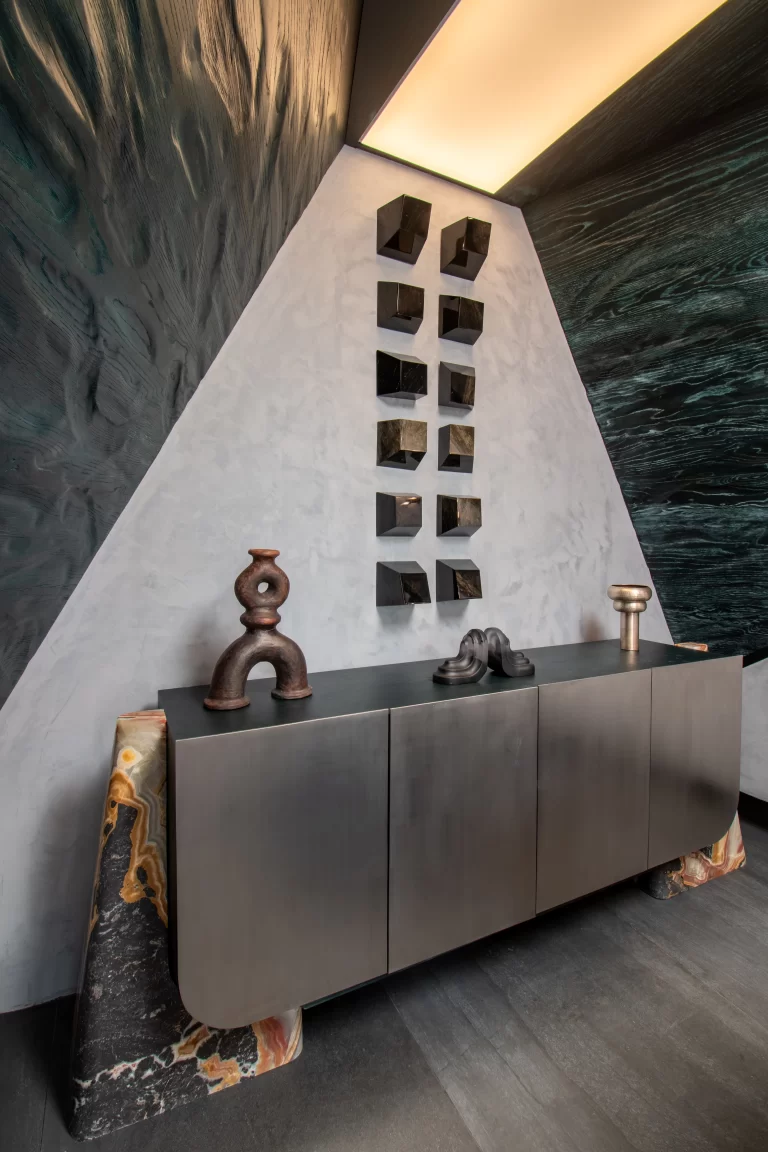 Muro con piezas de obsidiana empotradas sobre mueble bajo de acero inoxidable